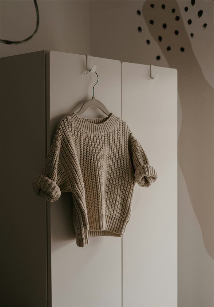 Sand-coloured knit jumper hanging on a hook